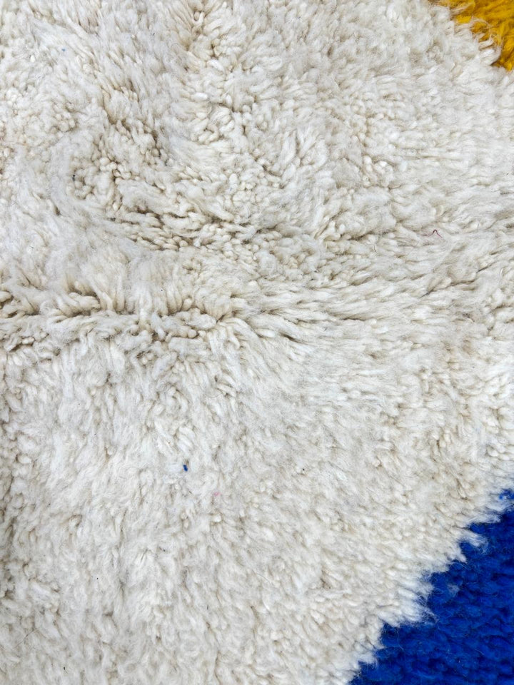 Round colorful Moroccan wool rug with abstract geometric shapes in pink, green, blue, and yellow.