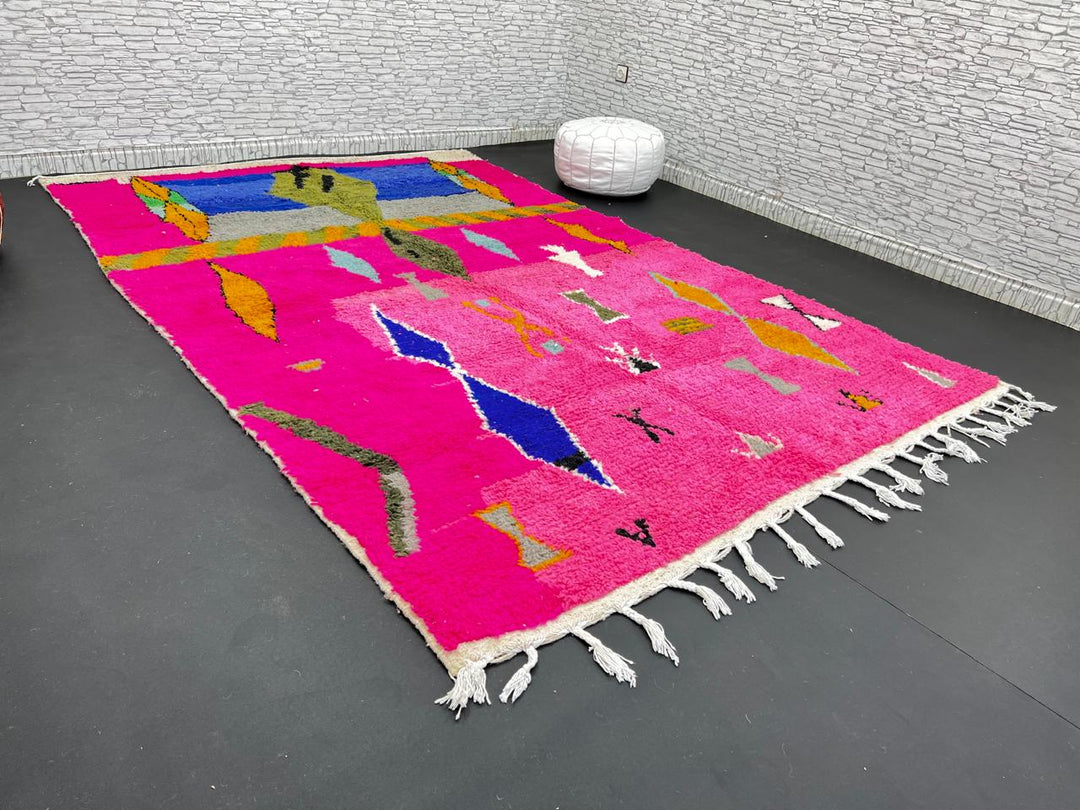 Handwoven colorful Moroccan wool rug with pink base and abstract blue, green, orange, and gold tribal motifs