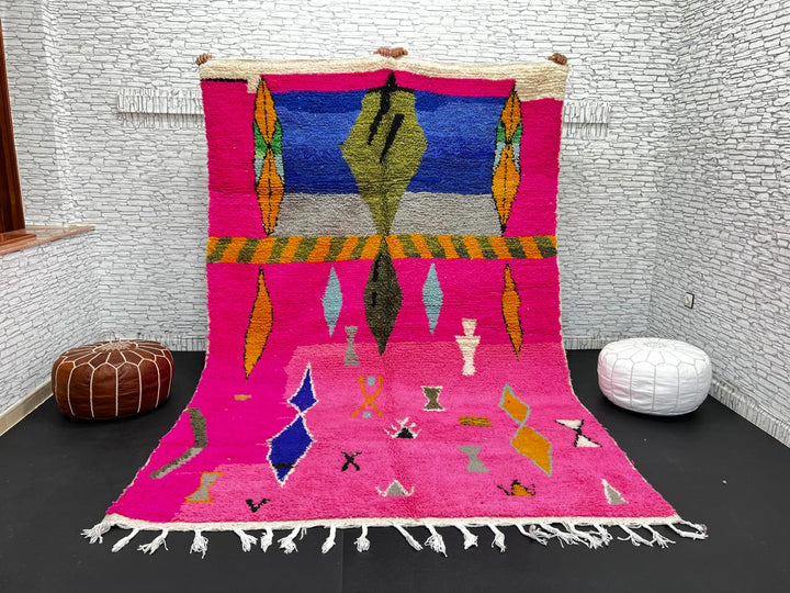 Handwoven colorful Moroccan wool rug with pink base and abstract blue, green, orange, and gold tribal motifs