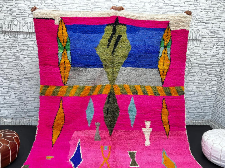 Handwoven colorful Moroccan wool rug with pink base and abstract blue, green, orange, and gold tribal motifs