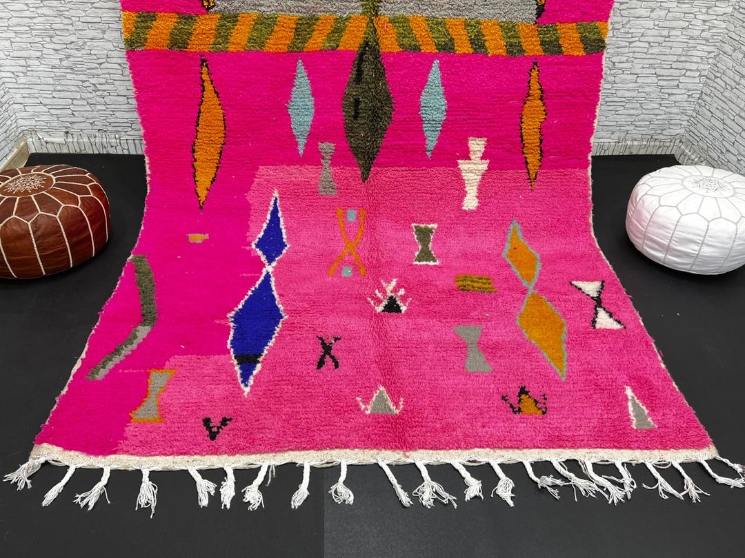 Handwoven colorful Moroccan wool rug with pink base and abstract blue, green, orange, and gold tribal motifs