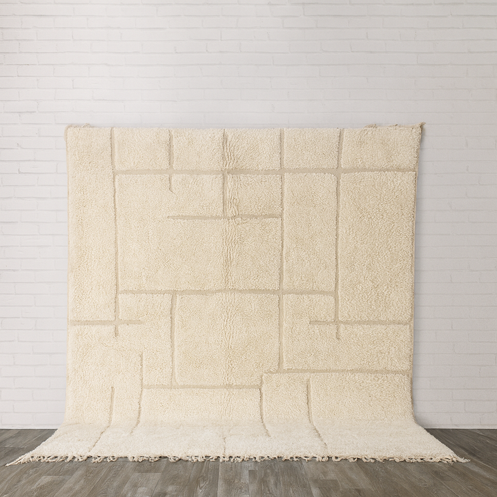 Cream moroccan rug  textured blanket on a wooden floor with a light gray wall background