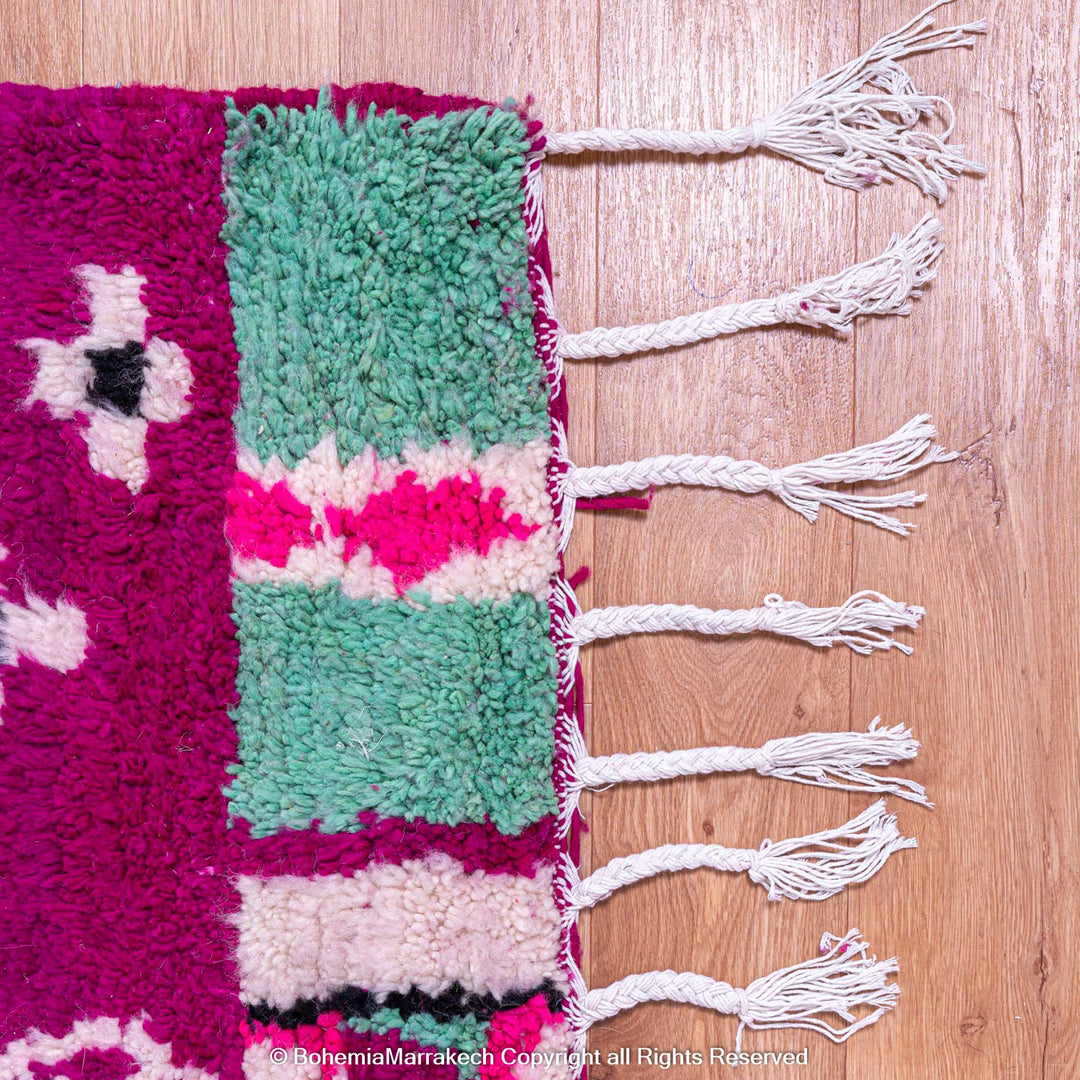 Pink Azilal Moroccan wool rug with colorful geometric tribal designs and tassels, handcrafted by Berber artisans.