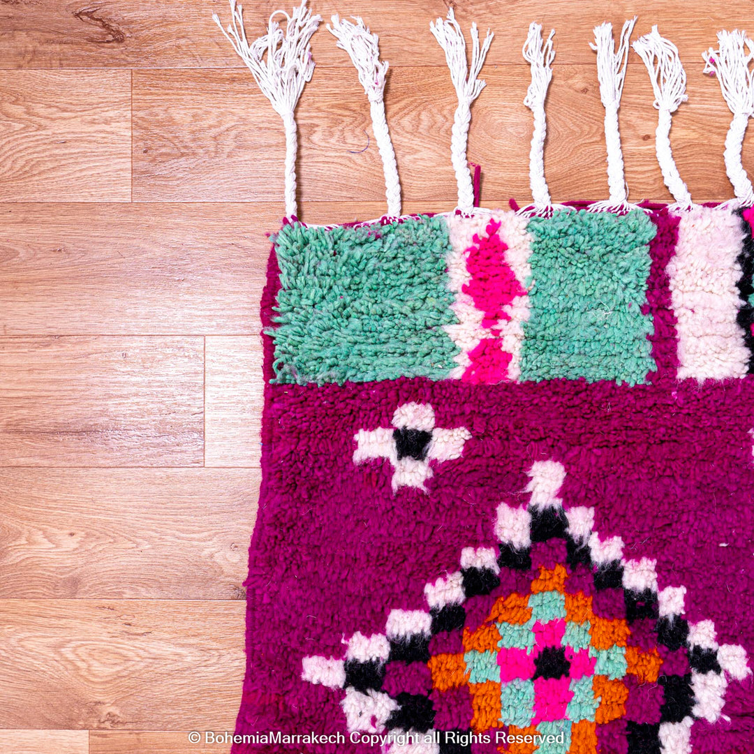 Pink Azilal Moroccan rug with colorful tribal wool patterns on wooden floor.