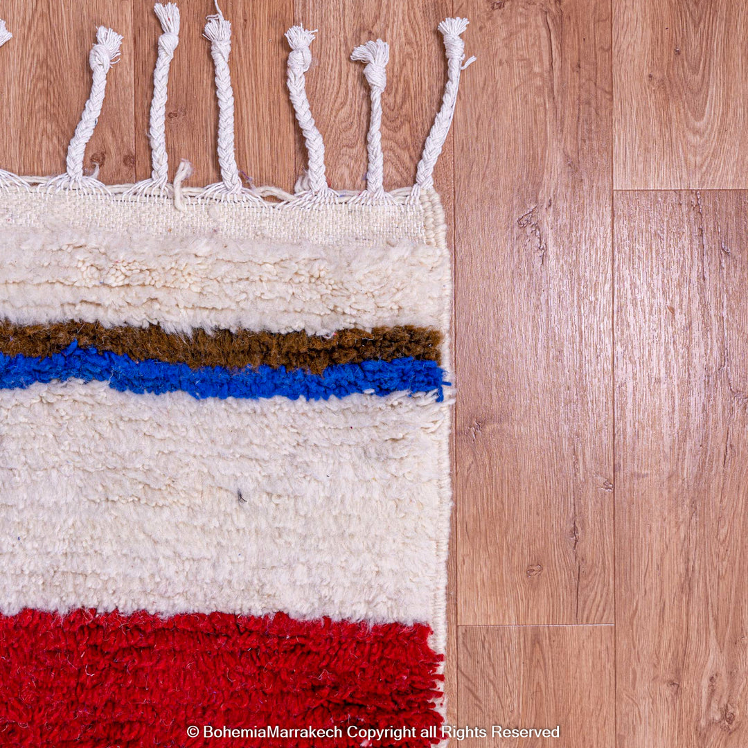 Colorful Moroccan wool rug with geometric stripes in red, blue, and brown on ivory, showcasing traditional Berber design.