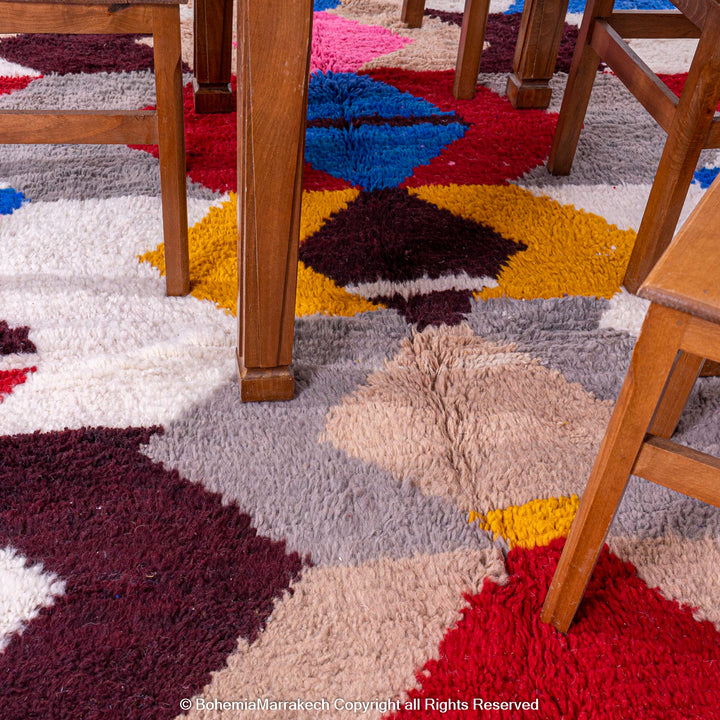 Colorful geometric Azilal rug beneath wooden dining chairs, showcasing vibrant diamond patterns. Moroccan wool area rug for eclectic decor.