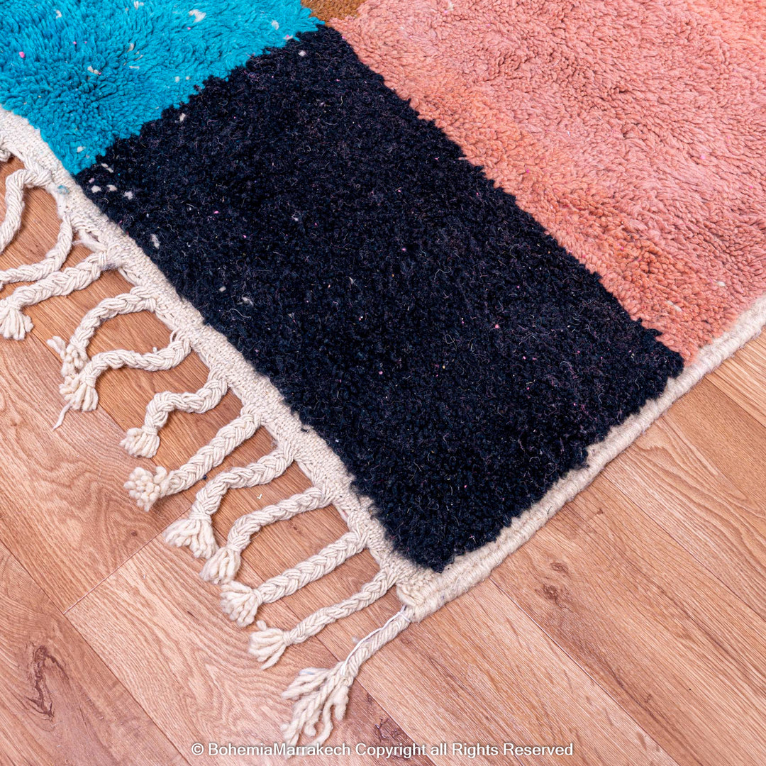 Colorful handmade Moroccan rug with geometric design, featuring vibrant pink, blue, and black wool on a wood floor.