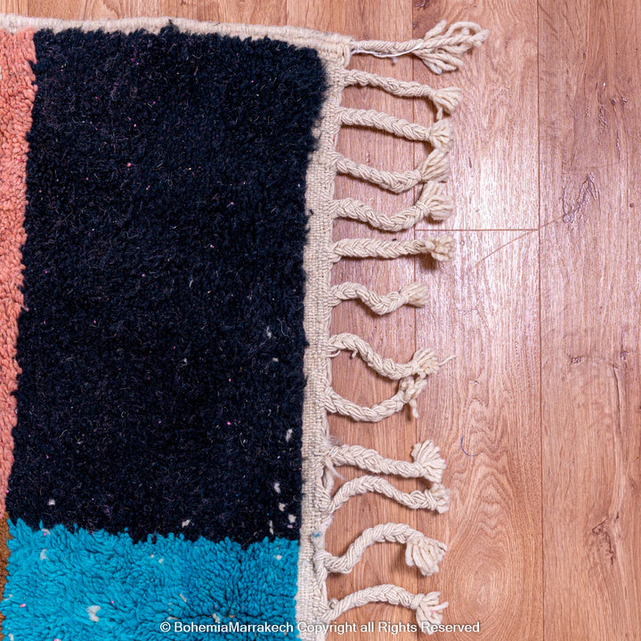 Close-up of colorful handmade Moroccan wool shag rug with geometric design on a wooden floor.
