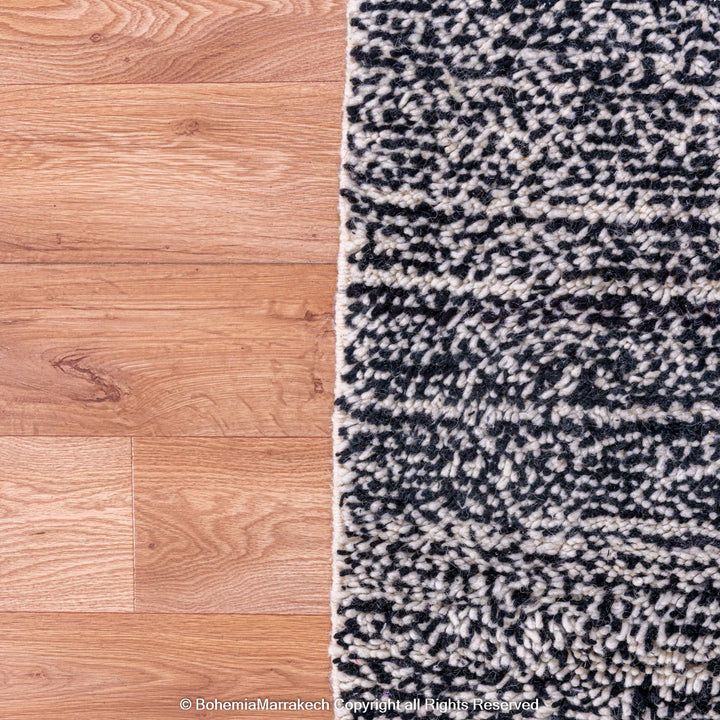 Grey Moroccan Beni Ourain wool rug on hardwood floor, showcasing marbled dark grey and white tones for modern interiors.
