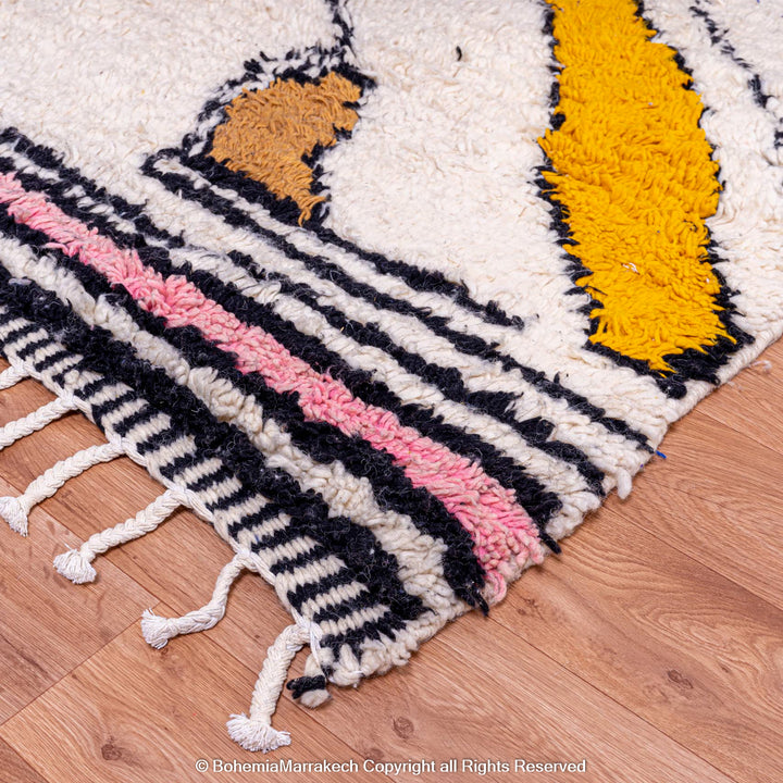 Colorful Abstract Moroccan Berber Rug with Zigzag Patterns, Handmade Wool Rug in Blue, Pink, Yellow, and Brown, on Wooden Floor.