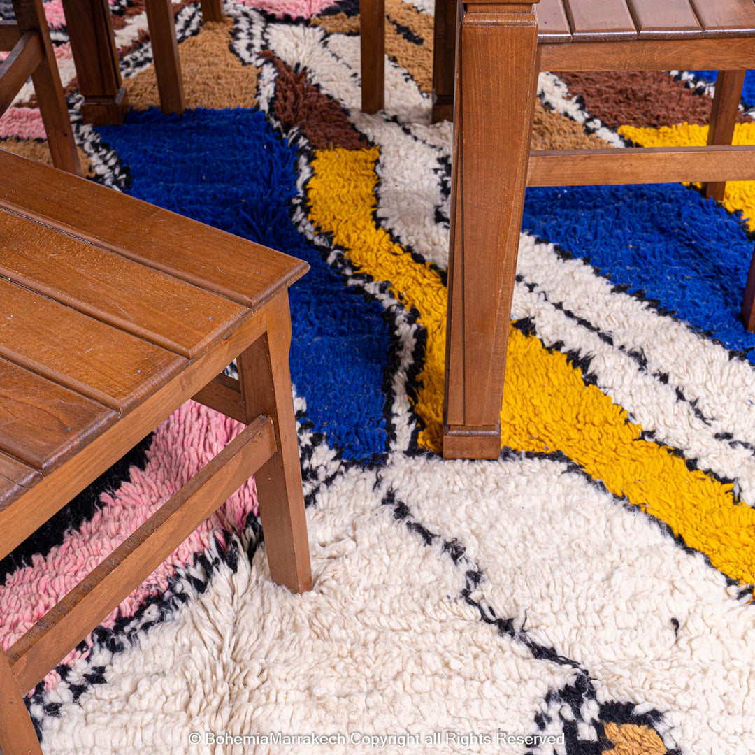 Colorful Abstract Moroccan Berber Rug with vibrant zigzag patterns in blue, mustard, pink under wooden furniture.