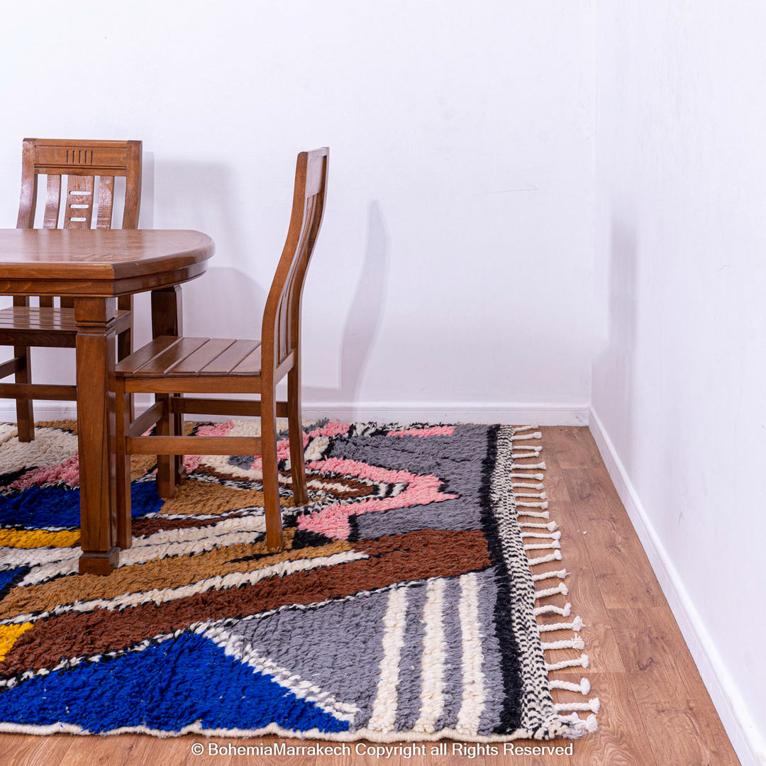 Colorful Abstract Moroccan Berber Rug under dining set, featuring bold patterns in blue, mustard yellow, and brown on wooden floor.