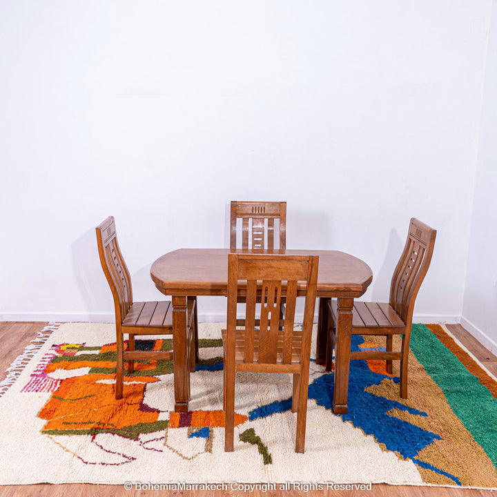 Colorful Moroccan rug featuring abstract camel design under a wooden dining set, handcrafted by Berber artisans.