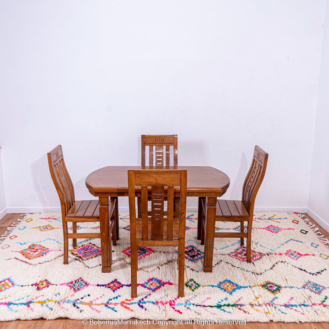 Colorful Moroccan rug with diamond Berber pattern under wooden dining set, featuring vibrant pink, blue, yellow, on cream base.