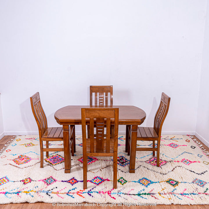 Colorful Moroccan rug with diamond Berber pattern under wooden dining set, featuring vibrant pink, blue, yellow, on cream base.