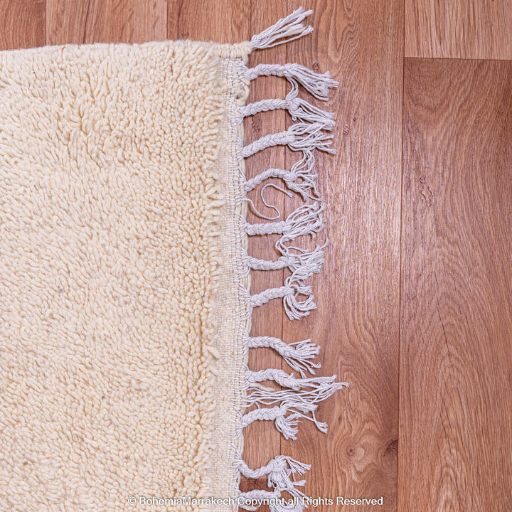 Fringe detail of a beige Moroccan wool rug on wooden floor, showcasing handwoven craftsmanship.