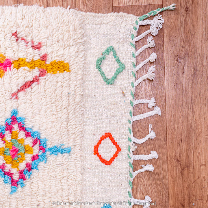 Colorful Moroccan rug with diamond Berber pattern in pink, blue, and orange on a cream base, showcasing intricate handmade design.