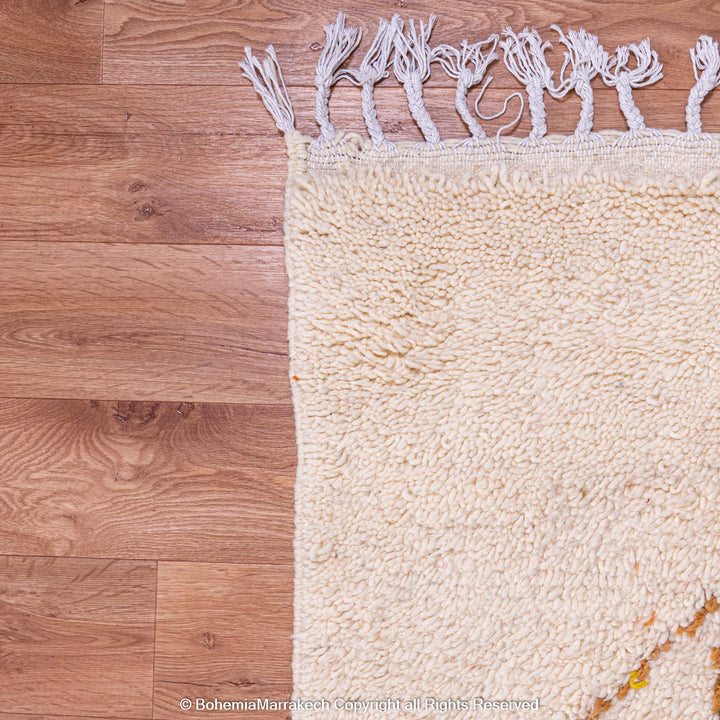 Close-up of a traditional Moroccan wool rug on wooden floor, showcasing intricate weave and fringe detailing.