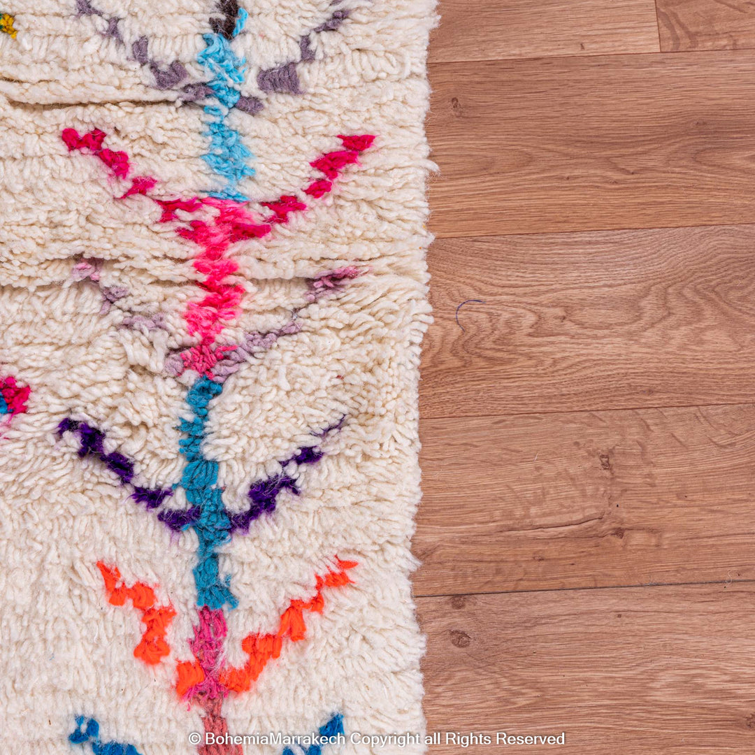 Colorful Moroccan rug with diamond Berber pattern, featuring vibrant pink, blue, and orange on a cream wool base.