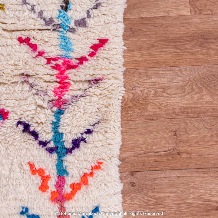 Colorful Moroccan rug with diamond Berber pattern, featuring vibrant pink, blue, and orange on a cream wool base.