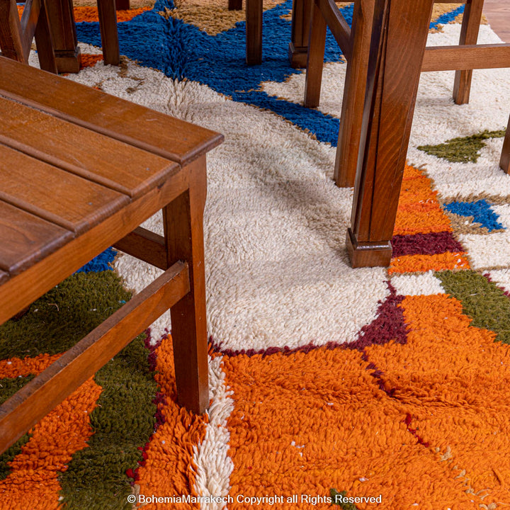 Colorful Moroccan rug with abstract camel design under wooden furniture in a dining room setting.