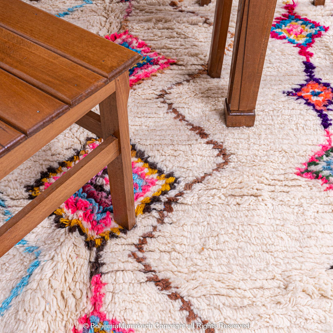 Colorful Moroccan Berber rug with diamond pattern under a wooden chair, featuring pink, blue, and orange on a cream base.
