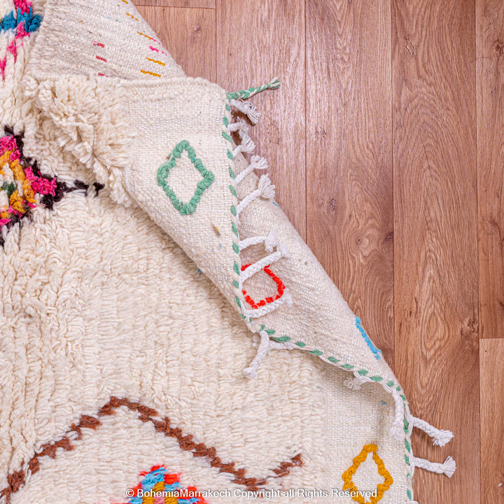 Colorful Moroccan rug with diamond Berber pattern, handmade with natural wool, showcasing pink, blue, and orange accents on a cream background.