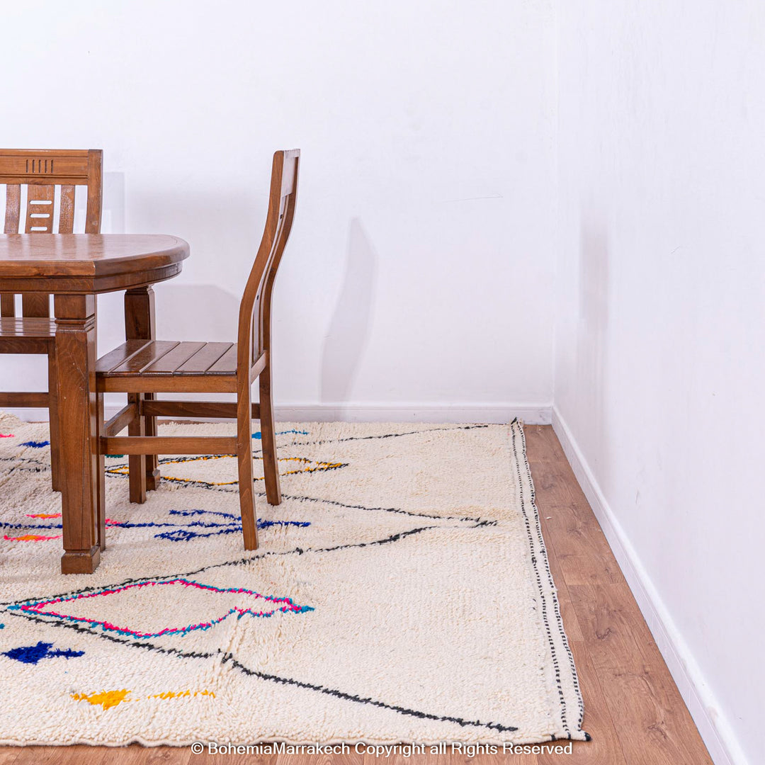 Colorful Azilal Moroccan wool rug with tribal designs, under wooden dining table on wooden floor.