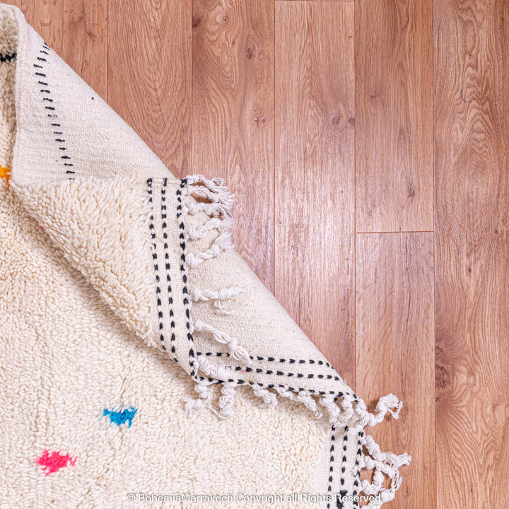 Colorful Azilal Moroccan rug with fringed edge and diamond motifs on wood floor - traditional wool carpet from Morocco.