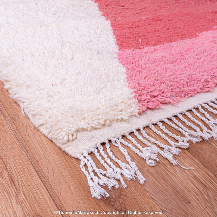 Red and pink handmade Moroccan wool rug with hourglass design on wooden floor.