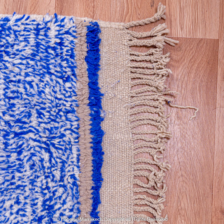 Blue and white Moroccan wool rug with fringe edges on wooden floor