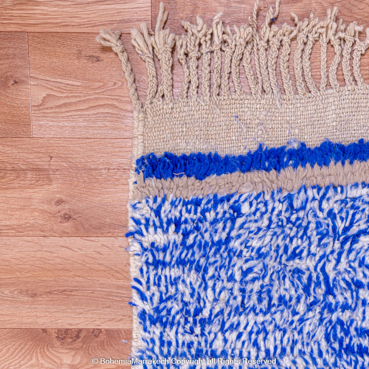 Blue and beige Moroccan wool rug with fringe on hardwood floor.
