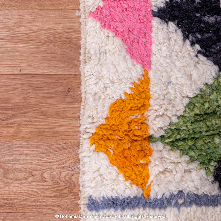 Colorful Moroccan rug with geometric shapes and vibrant colors like pink, tangerine, and green on a white wool base.