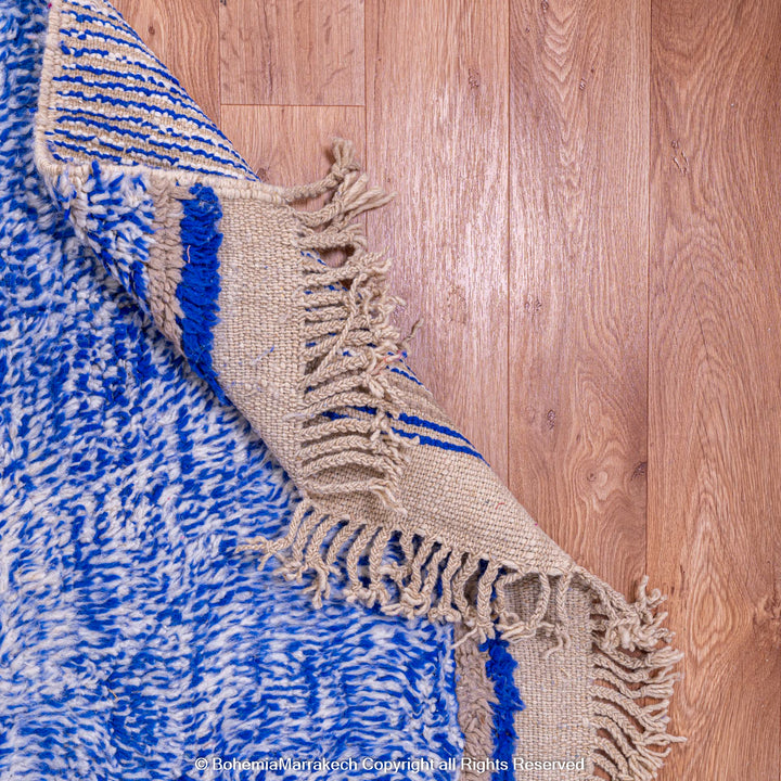 Blue and white Moroccan rug with fringed edges on wooden floor
