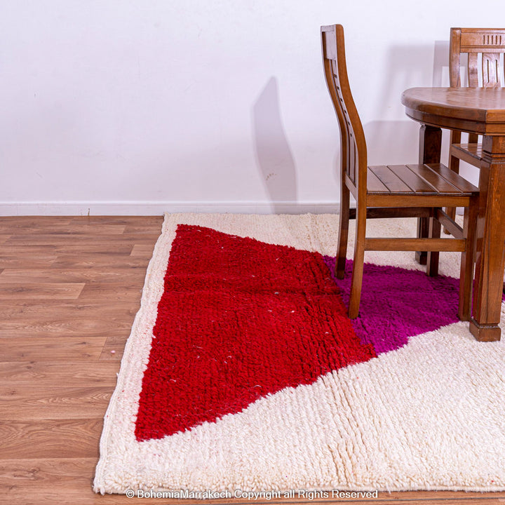 Red and pink handmade Moroccan wool rug under wooden dining set, showcasing vibrant hourglass design.