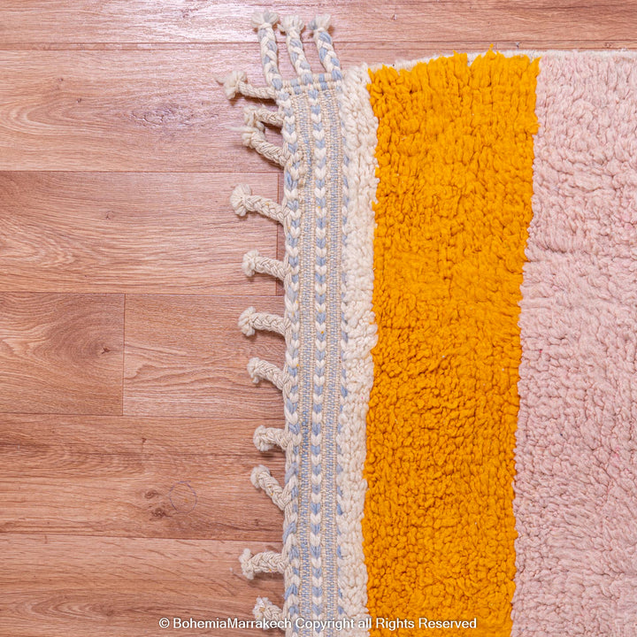 Handmade Moroccan wool rug with colorful stripes and fringe on hardwood floor, traditional Berber craftsmanship.