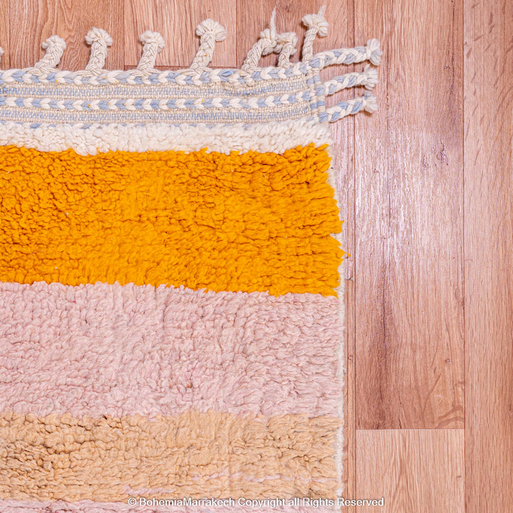 Handmade Moroccan rug with colorful stripes in wool, featuring orange, pink, and beige hues on wooden flooring.