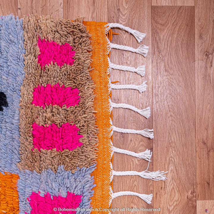 Abstract Moroccan wool rug with vibrant geometric patterns in pink, blue, orange, and natural wool, handwoven by Berber women.