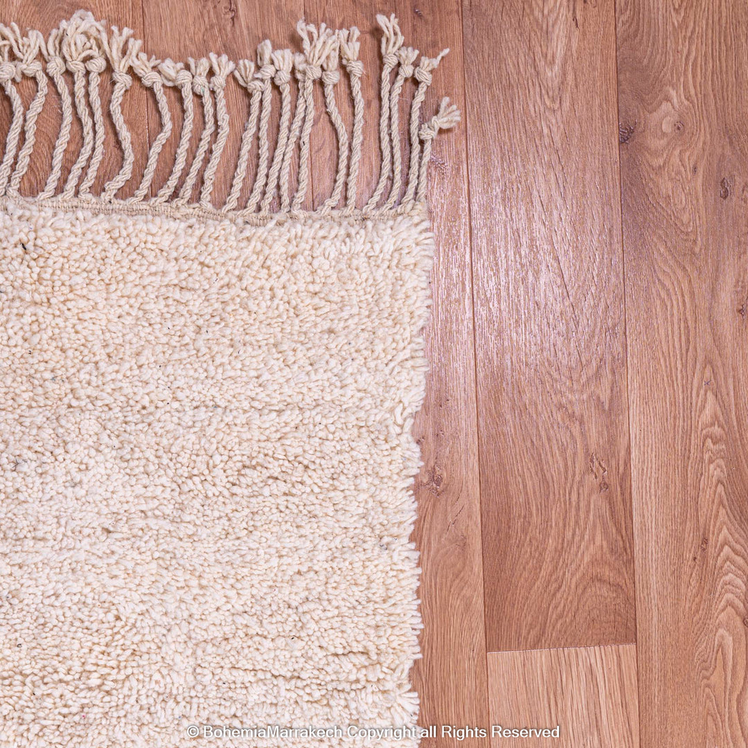 Close-up of a wool Moroccan shag rug with fringes on a wood floor.