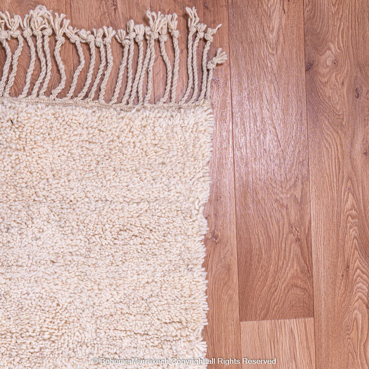 Close-up of a wool Moroccan shag rug with fringes on a wood floor.