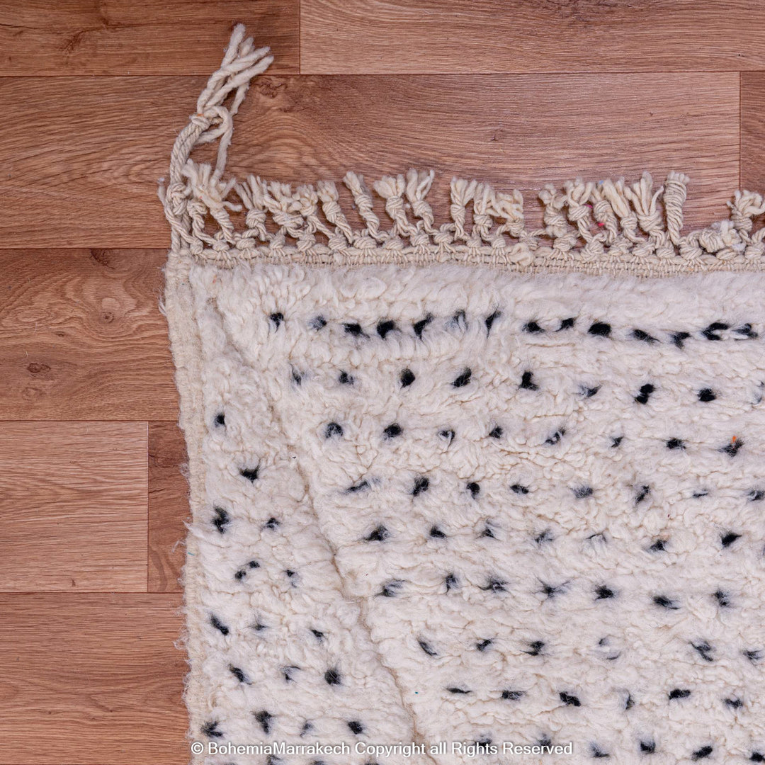 White Moroccan rug with black dots and diamond patterns on wooden floor, handwoven from natural wool. Perfect for Scandinavian interiors.