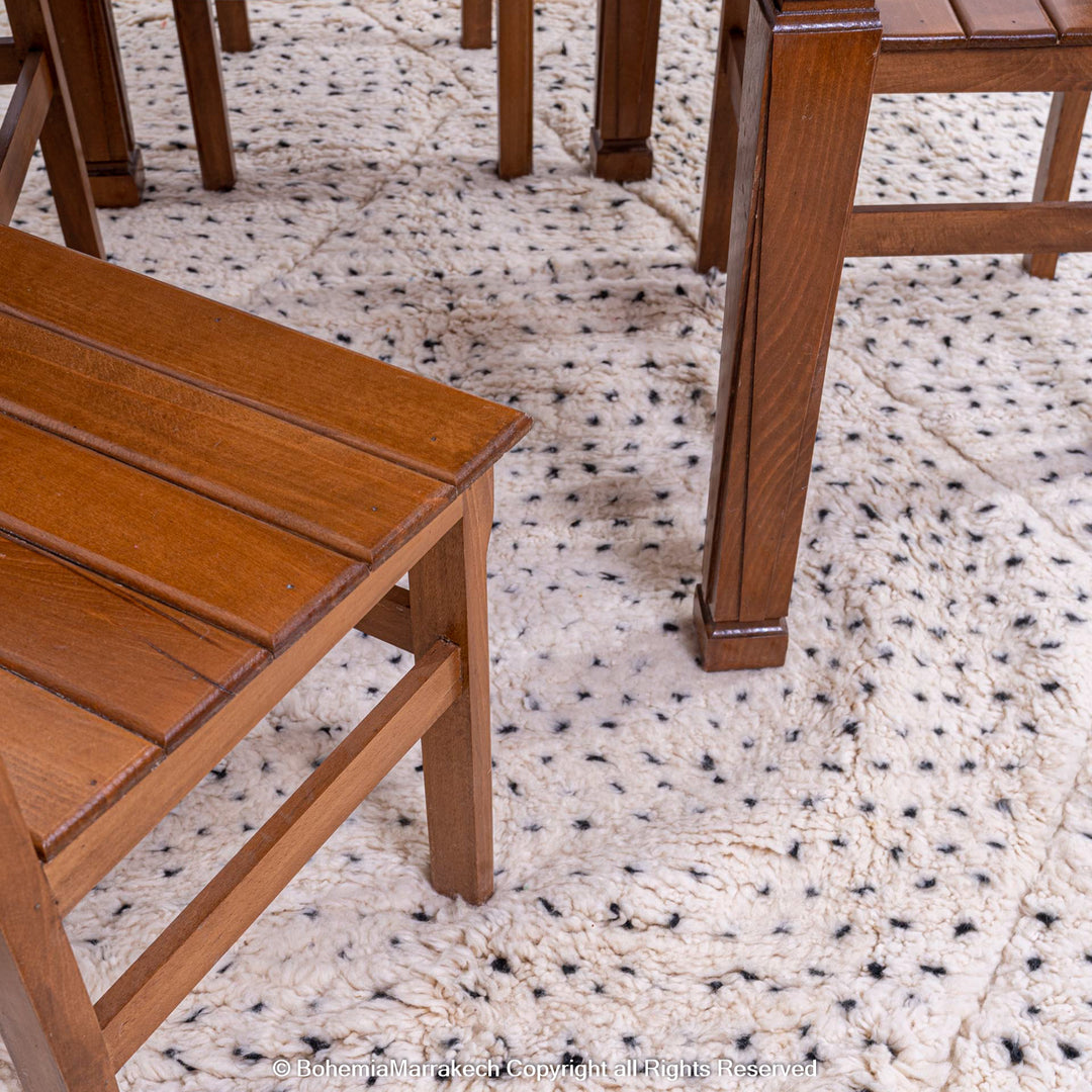 White Moroccan rug with black dots and diamond pattern under wooden chairs, handwoven wool, fits minimalist and boho interiors.