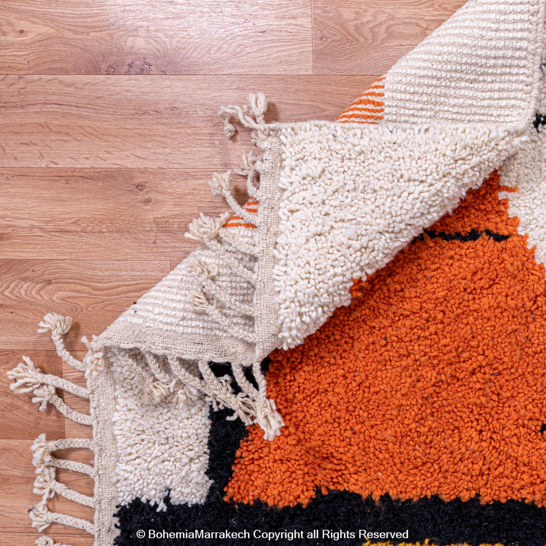 Abstract face Moroccan rug showcasing orange, black, and cream handwoven wool design on a wooden floor.