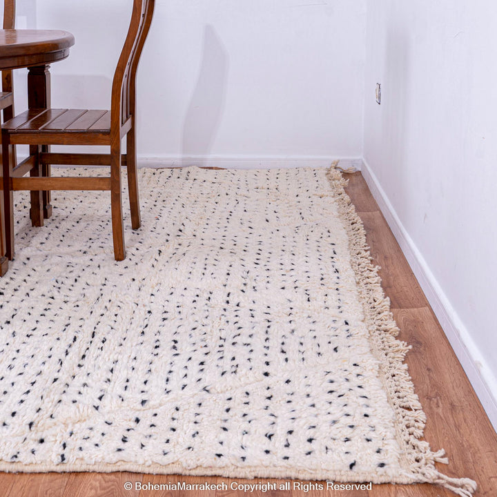 White Moroccan rug with black dots and diamond pattern on a wooden floor, ideal for boho and minimalist interiors.