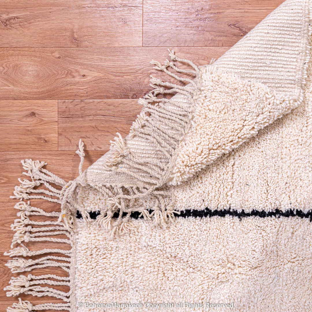 Close-up of a cream Moroccan wool rug with black line detail and fringed edges, showcasing a traditional handwoven design.