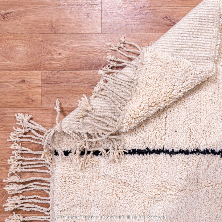 Close-up of a cream Moroccan wool rug with black line detail and fringed edges, showcasing a traditional handwoven design.