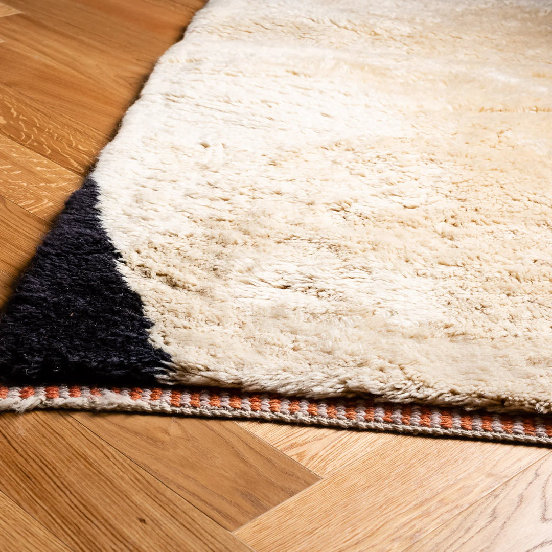 Custom Moroccan rug in ivory and black on hardwood floor, handwoven wool with traditional and contemporary design.