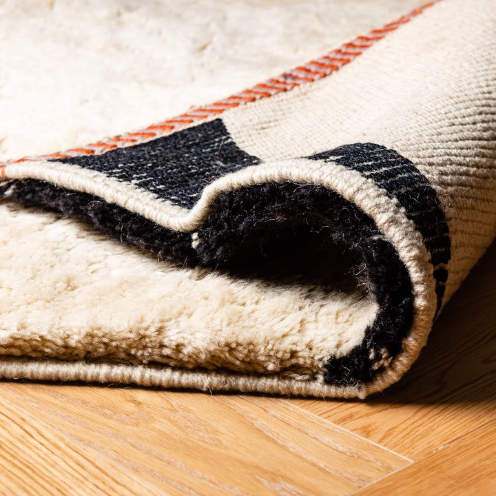 Custom Moroccan rug in terracotta, ivory, and black, showcasing rich texture and abstract design, handwoven wool, folded edge view.
