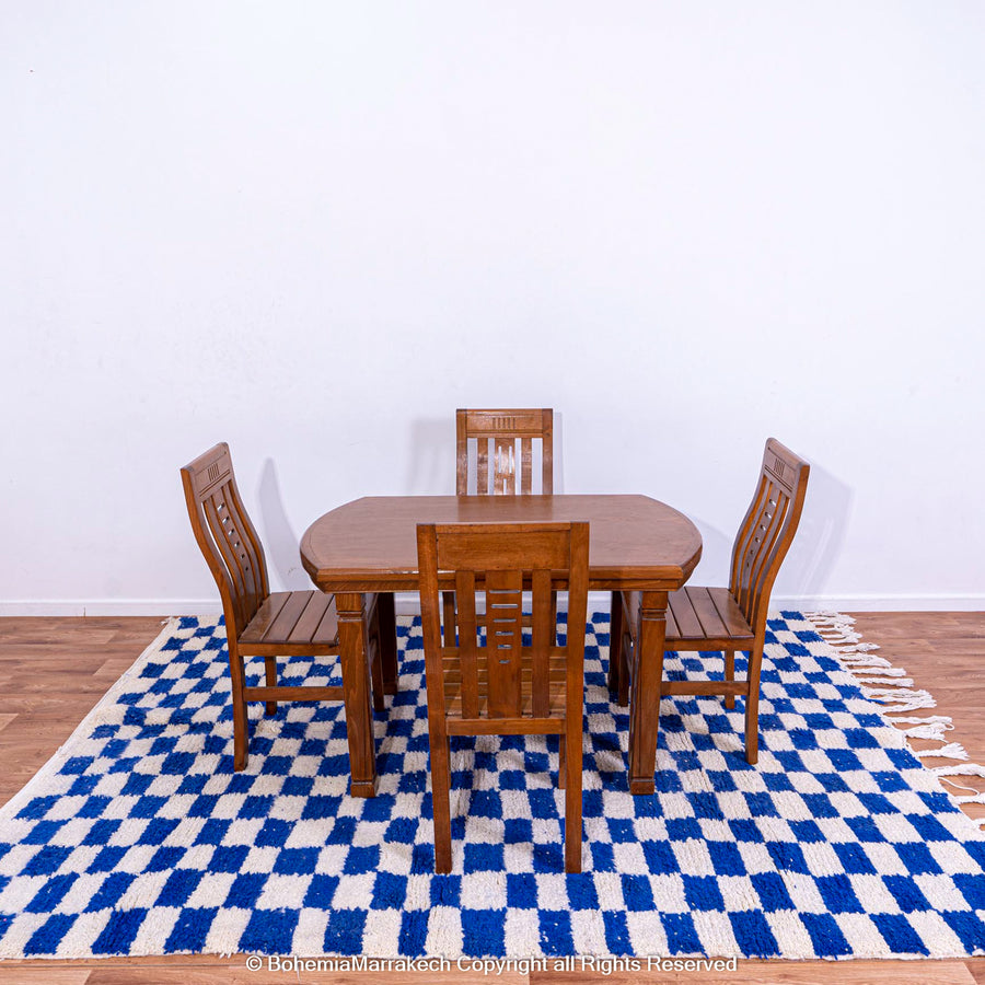 Handmade blue and white checkered Moroccan rug beneath a wooden dining set, showcasing traditional Berber craftsmanship.