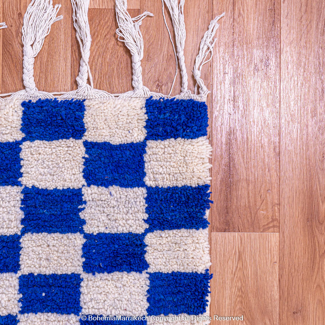 Blue and white checkered Moroccan wool rug with fringe, handcrafted by Berber artisans; perfect for eclectic and modern interiors.